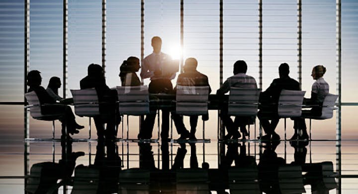 Silhouettes of people in a meeting room with a sunset backdrop.