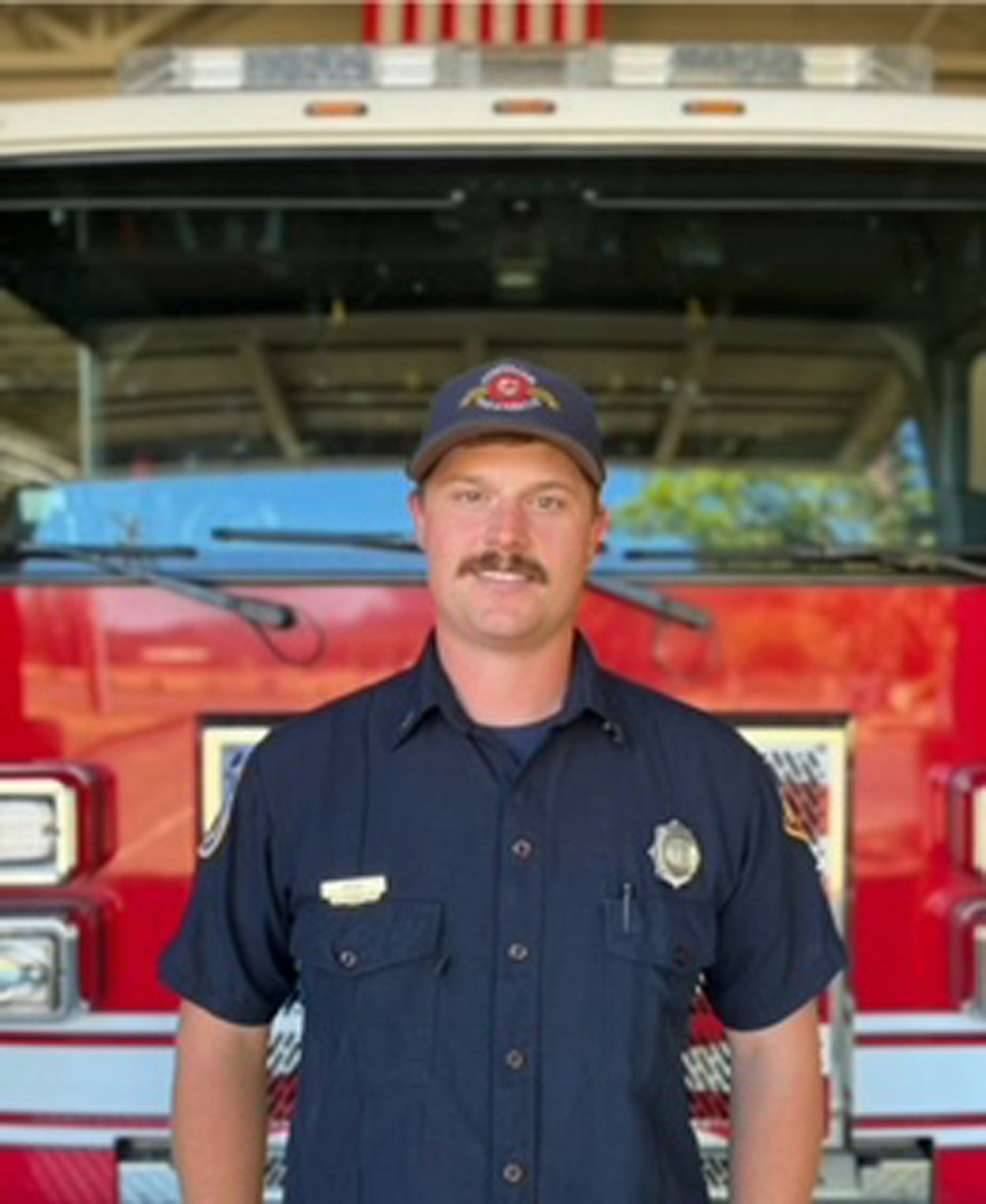 A firefighter in uniform standing in front of a fire truck.
