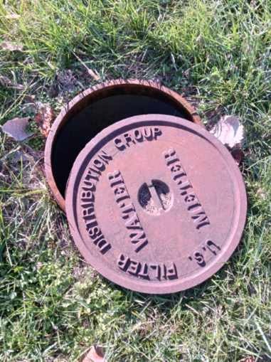 A partially opened manhole cover titled "U.S. WATER DISTRIBUTION GROUP FILTER."