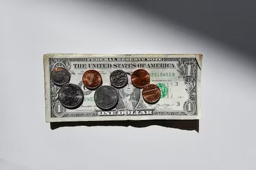 A one-dollar bill laid flat with various coins on top, including pennies, nickels, dimes, and quarters.