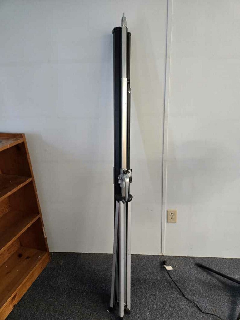 The image shows a tall, slim retractable stand, possibly for displaying signage or artwork, set against a wall.