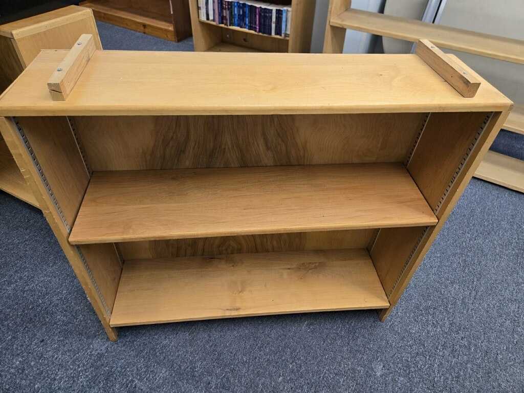 A wooden bookshelf with two shelves and a simple design, placed on a carpeted surface.