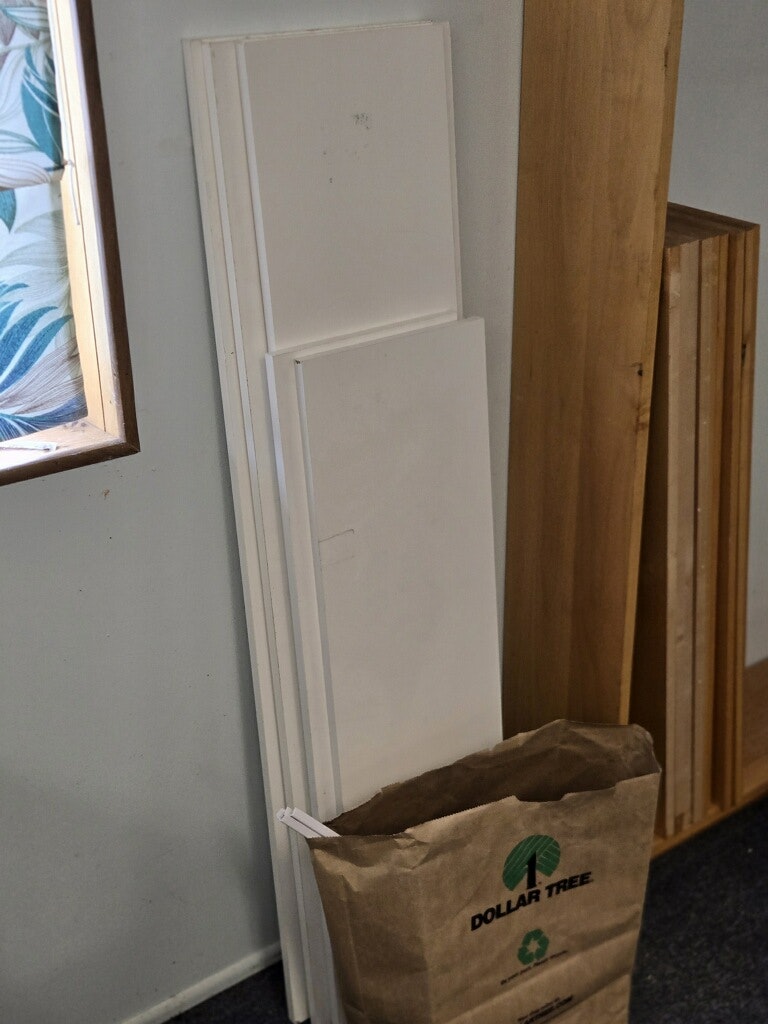 The image shows a stack of white panels leaning against a wall, with a Dollar Tree paper bag nearby.