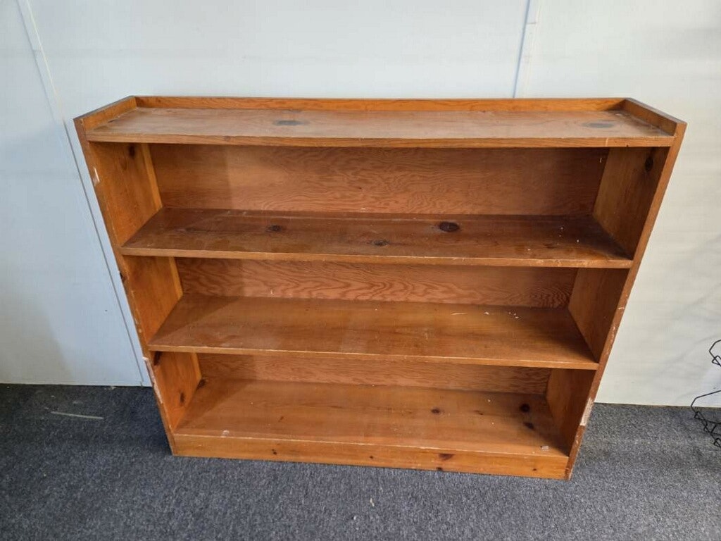 A wooden bookshelf with three open shelves, unfinished and empty, set against a neutral background.