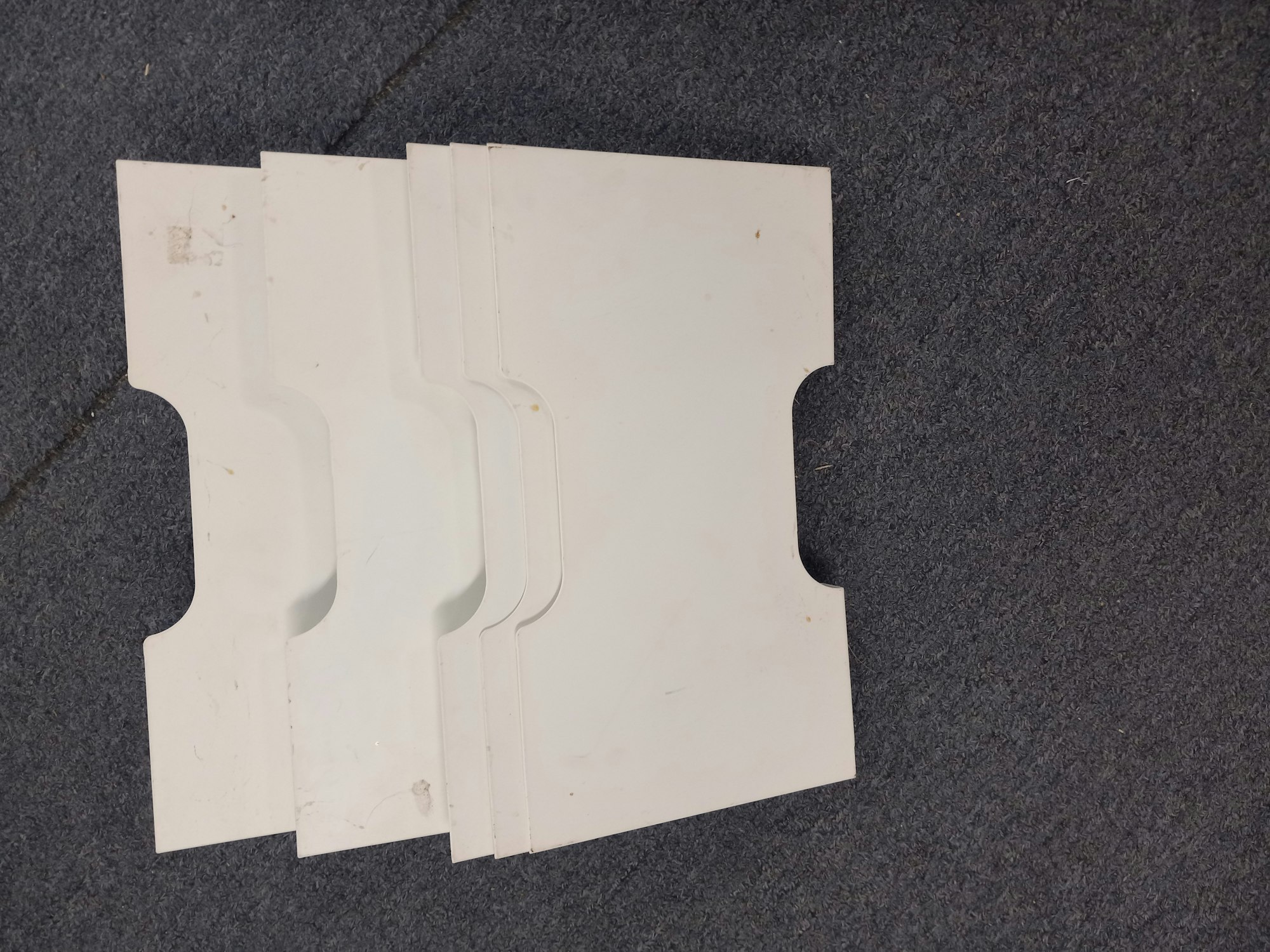 The image shows a stack of several white, plastic folders or file organizers on a gray carpet.