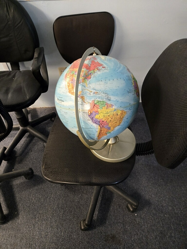 A globe sits on a chair, surrounded by other empty office chairs in a casual setting.