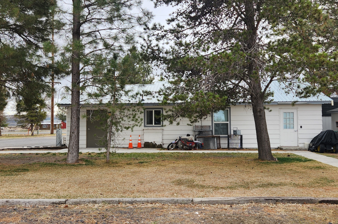 A single-story house with a metal roof, surrounded by trees, and featuring a motorcycle and traffic cones in the front yard.