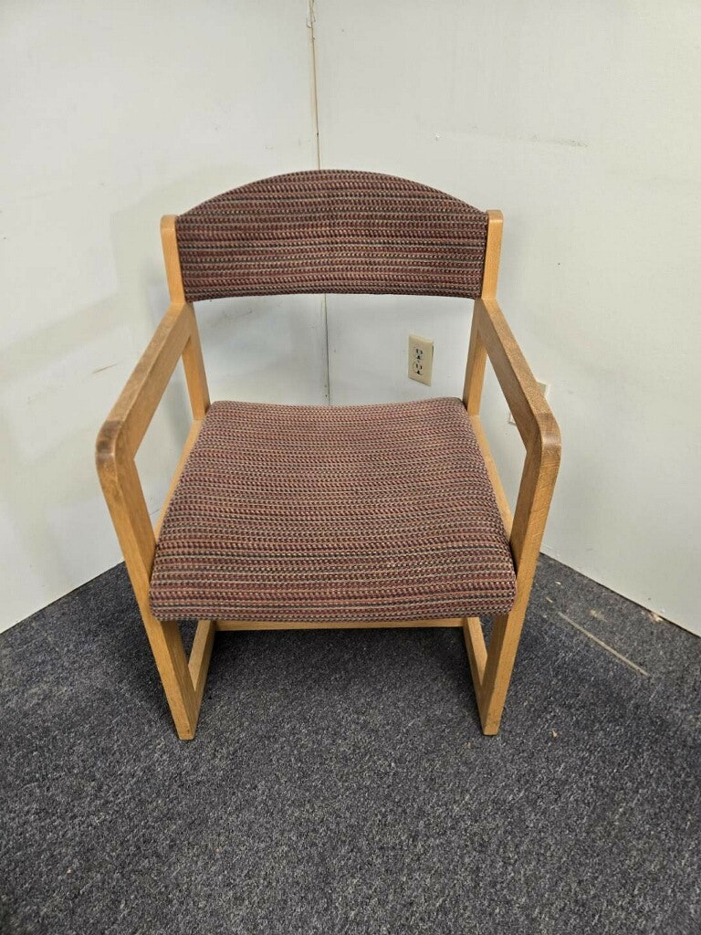 The image shows a simple, wooden-framed chair with a woven fabric seat and backrest, placed on a dark carpeted floor.