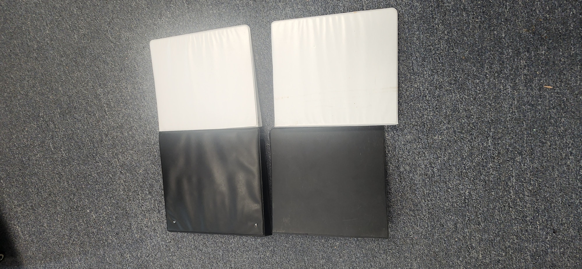The image shows two binders, one black and one white, laid flat on a textured surface.
