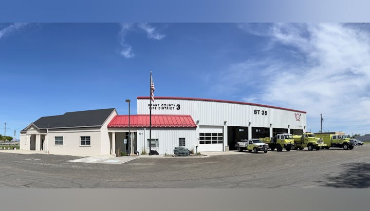 Fire station with several fire trucks parked outside, under a clear blue sky.