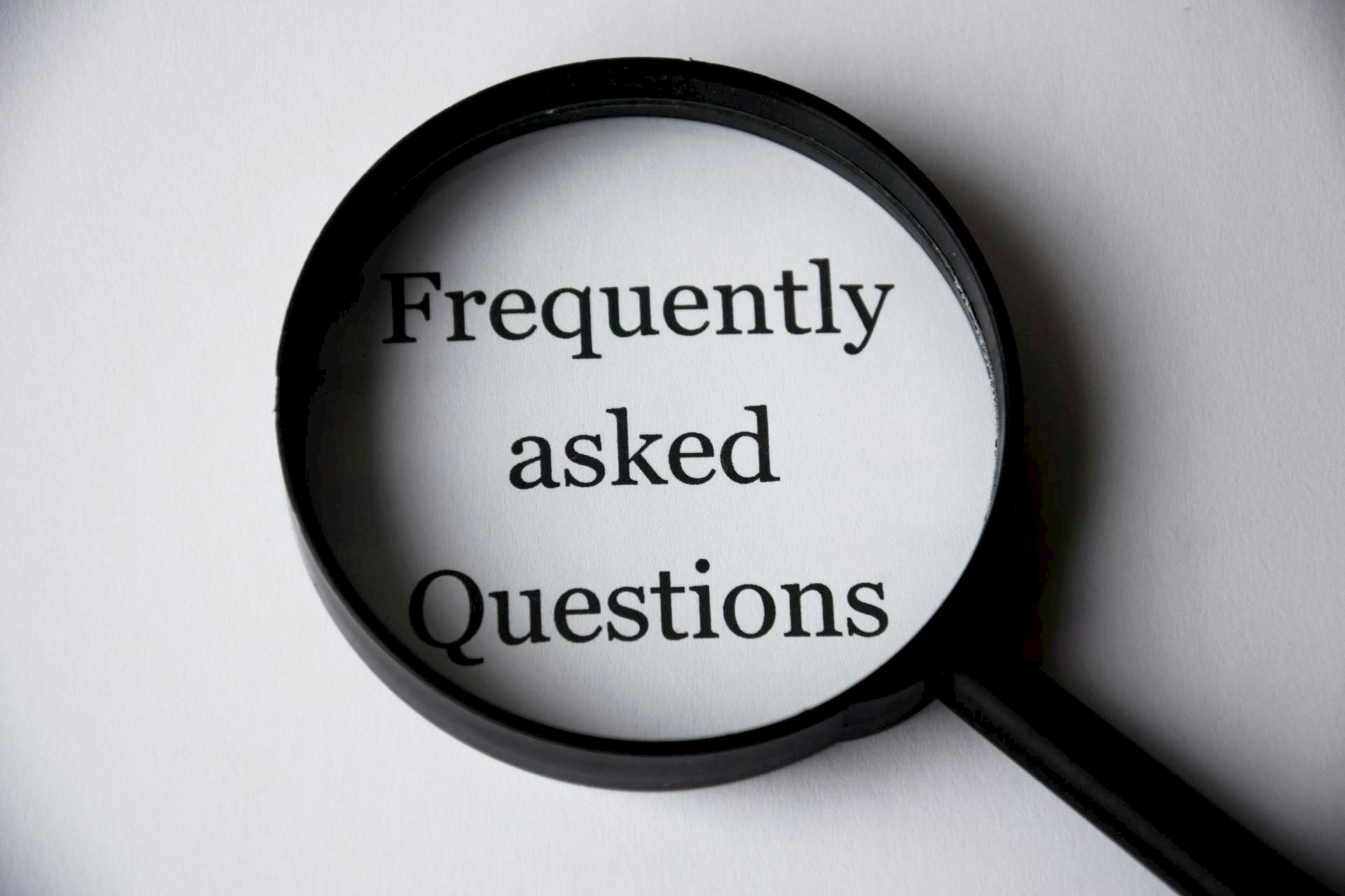 The image features a magnifying glass focusing on the text "Frequently asked Questions."