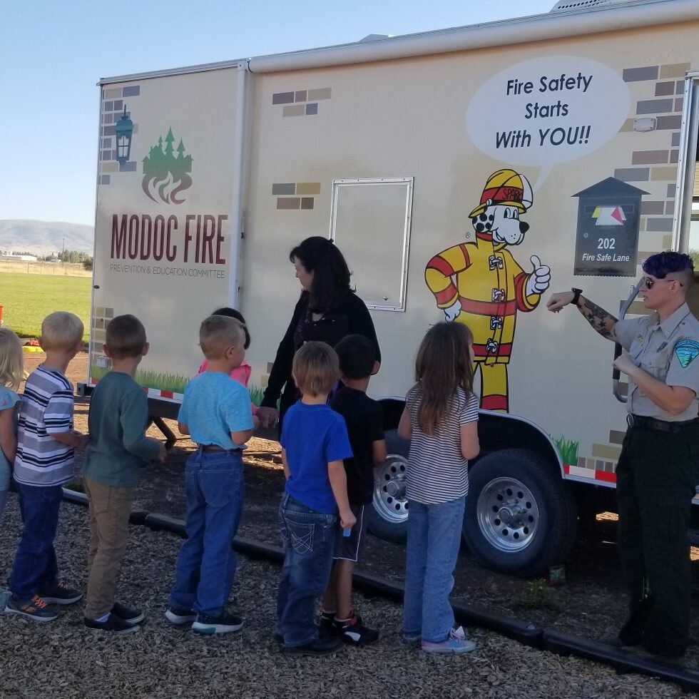 Children learn about fire safety from educators next to a Modoc Fire trailer.