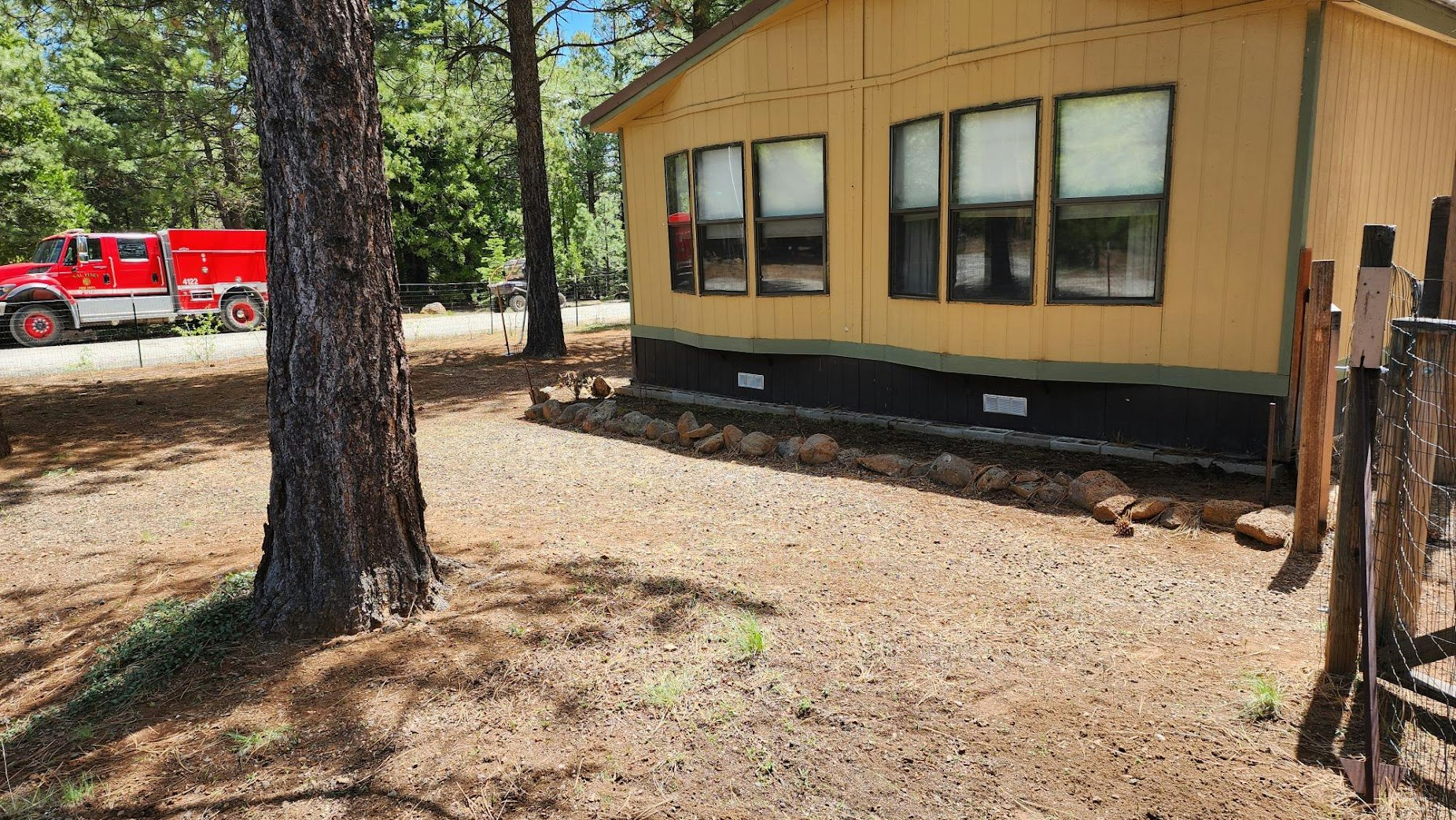 The image shows a yellow house with multiple windows, a large tree nearby, and a red truck in the background.