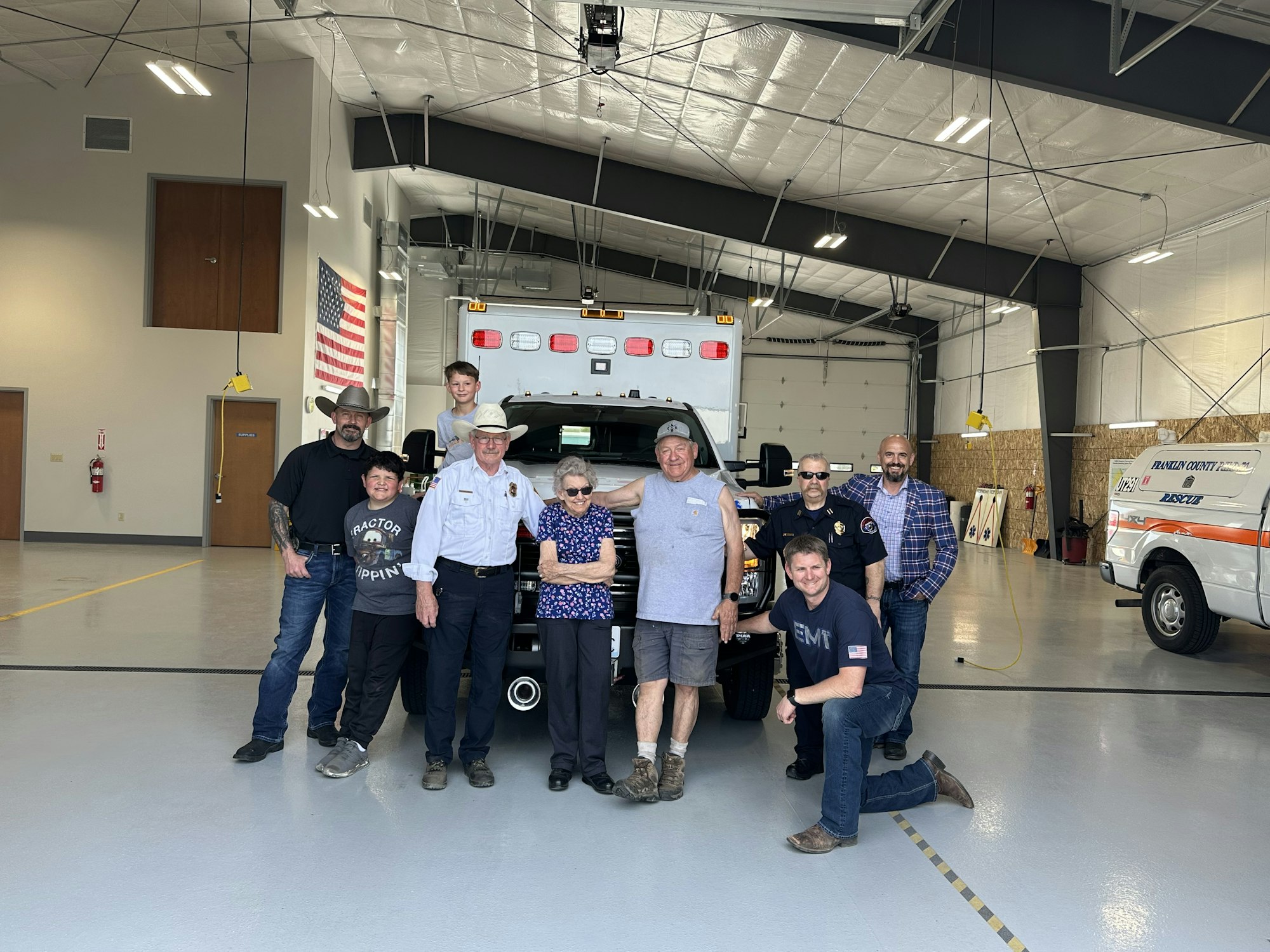 A group of people standing inside a garage or workshop with a vehicle and an American flag in the background.