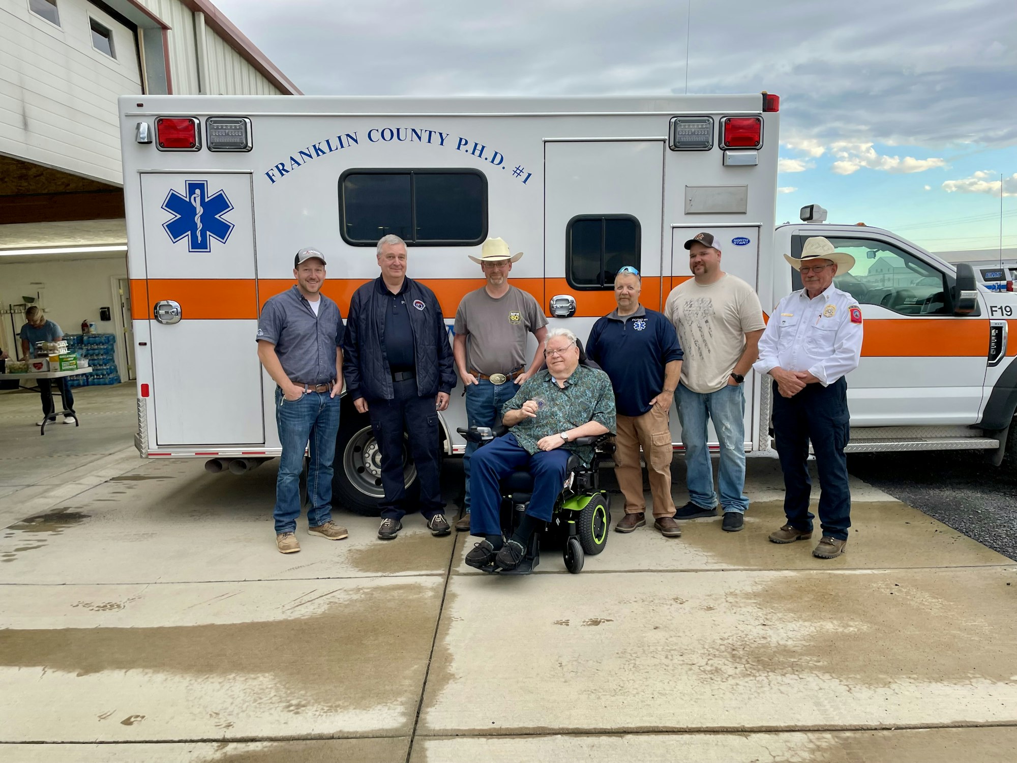 A group of seven men, one in a wheelchair, posing in front of a Franklin County ambulance.