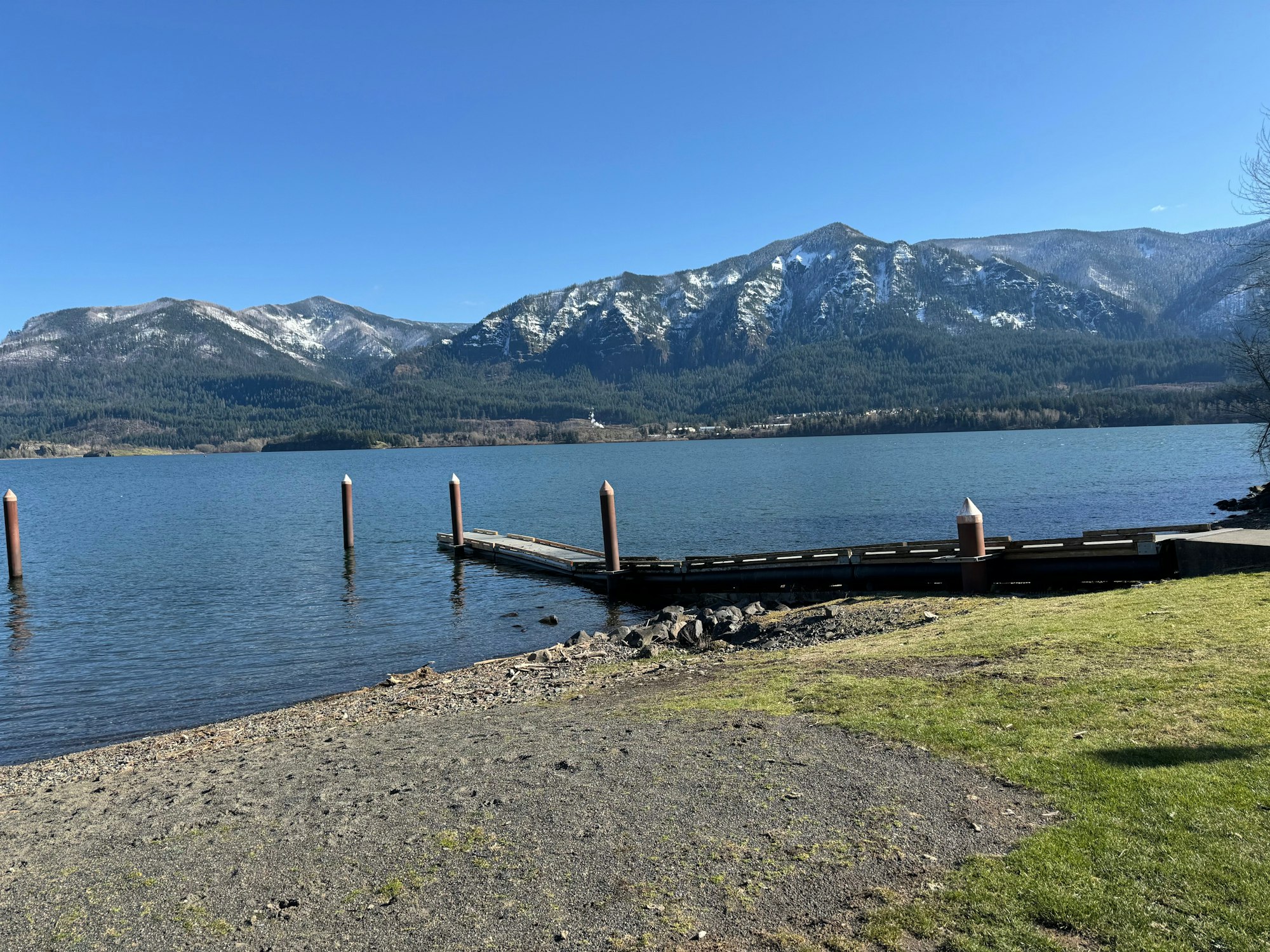 A serene lake with a dock, surrounded by mountains and clear skies.
