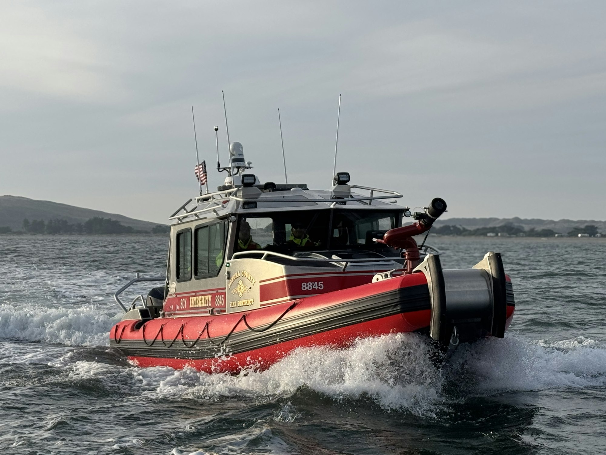 Red and gray rescue boat moving through water, with a hilly coastline in the background.