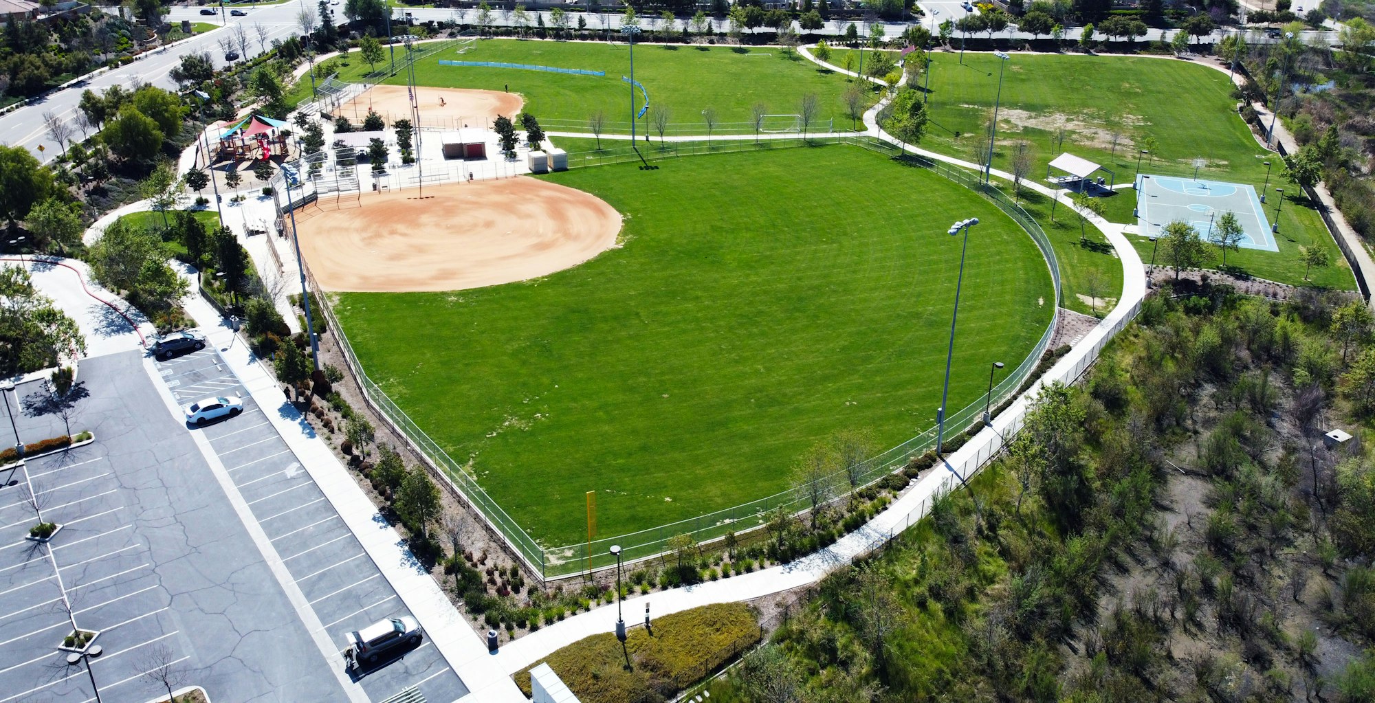 Spencer's Crossing Park, contains baseball fields, grass, basketball court, parking lot, playground, sidewalk