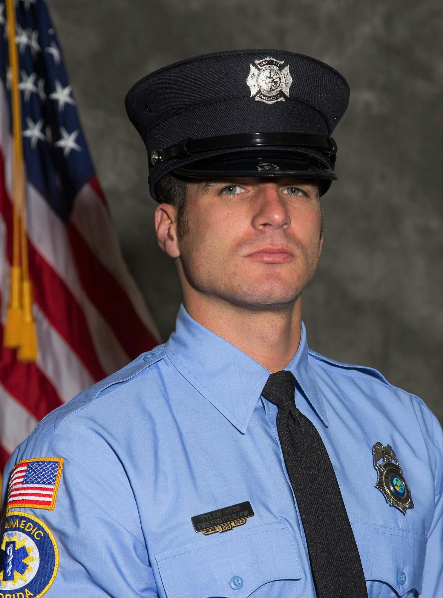 A firefighter in uniform poses in front of an American flag.