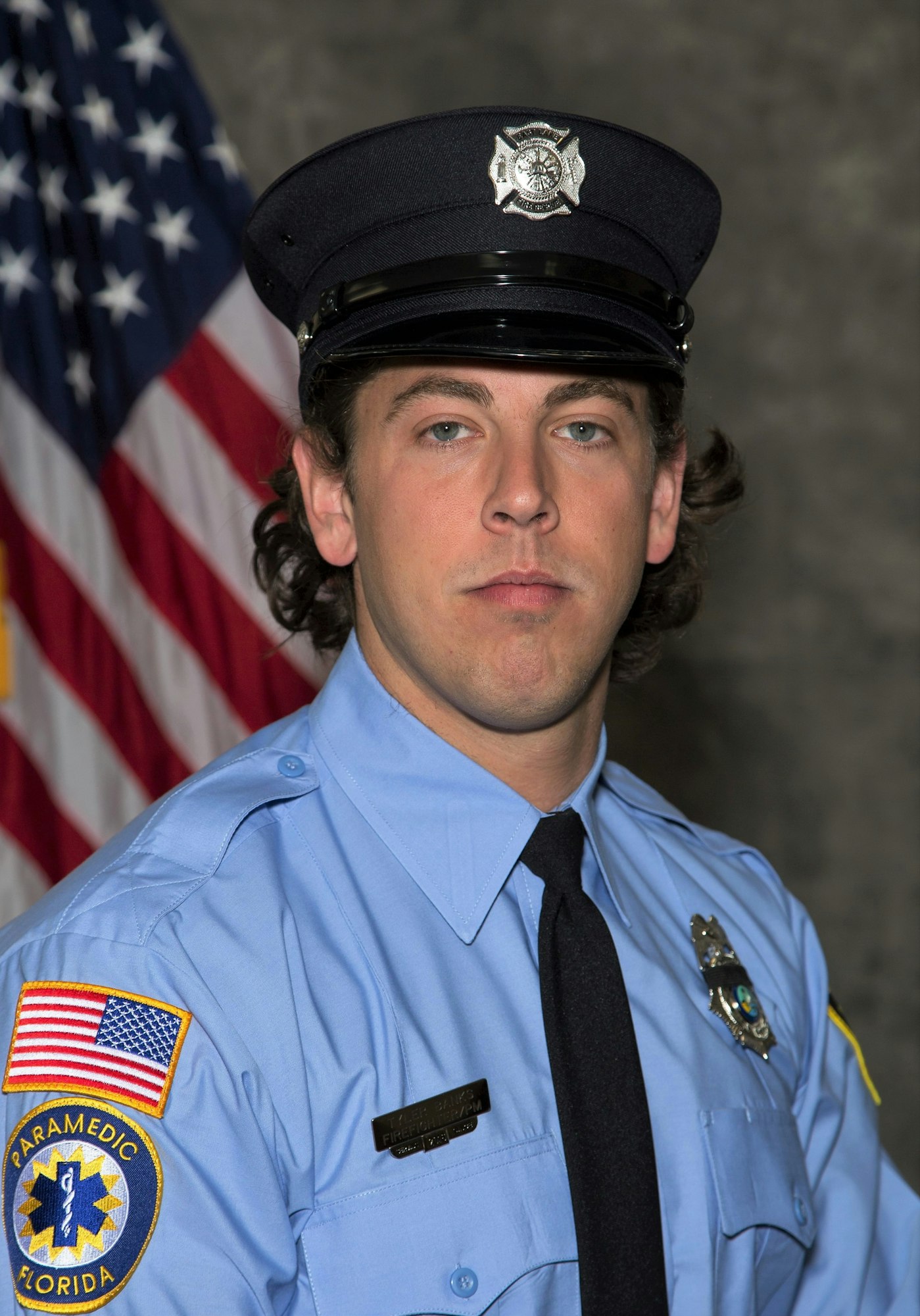 A person in a paramedic uniform with a badge and an American flag in the background.