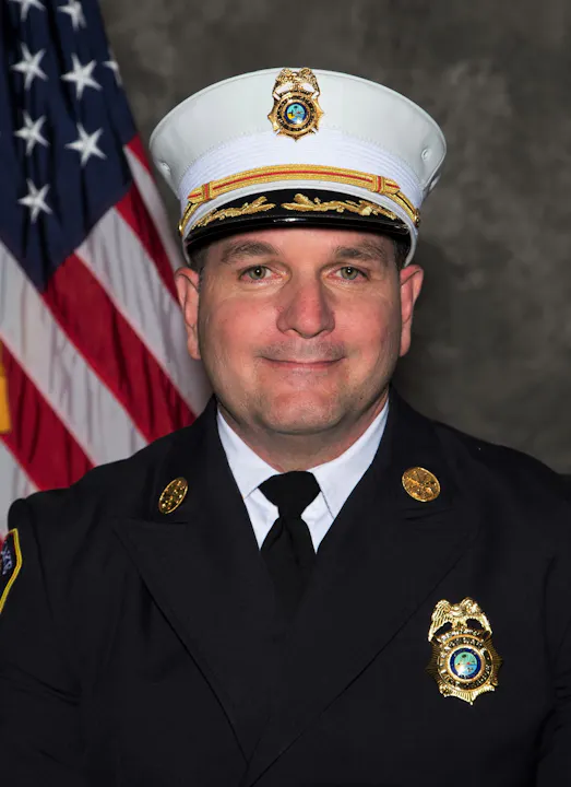 A uniformed officer smiles for a portrait, with an American flag in the background.