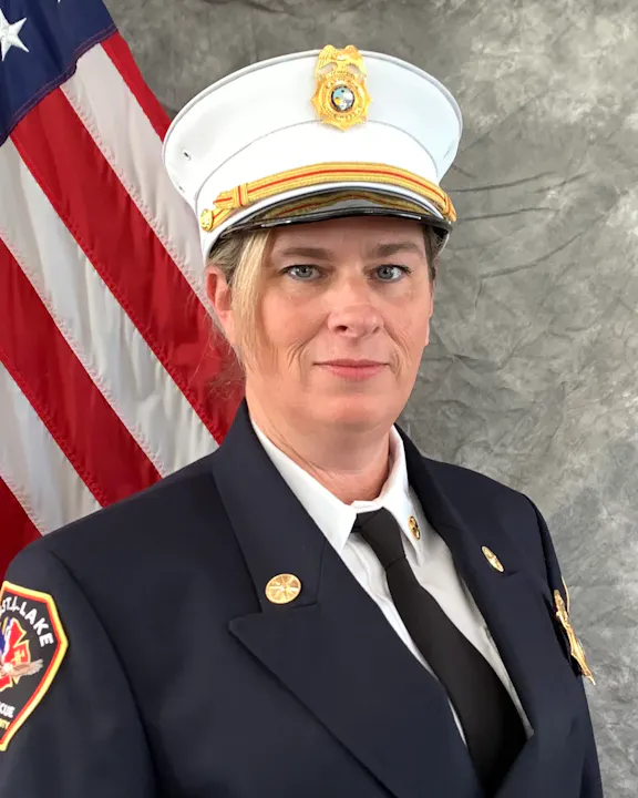 A person in a fire department uniform, standing in front of an American flag.