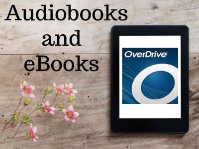 An e-reader displaying "OverDrive" rests on a wooden surface with text "Audiobooks and eBooks" and pink flowers nearby.