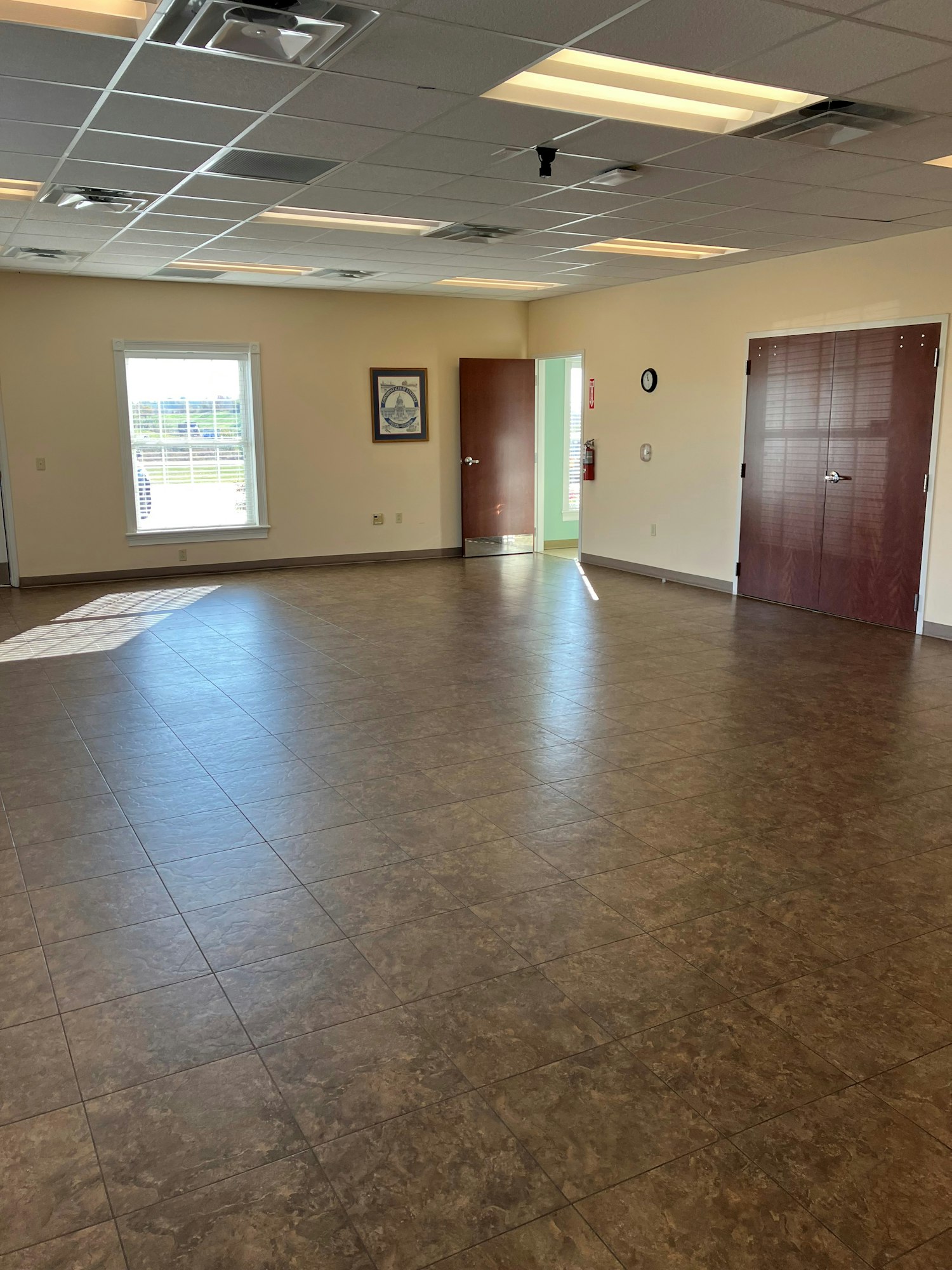 Community Room for events includes a spacious room for up to 60 people. This space has tan walls, multicolored brown tiled floor, and large windows on 2 walls.