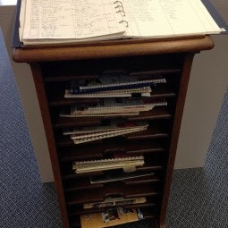 A wooden file organizer with shelves holding notebooks and papers, with a binder open on top.