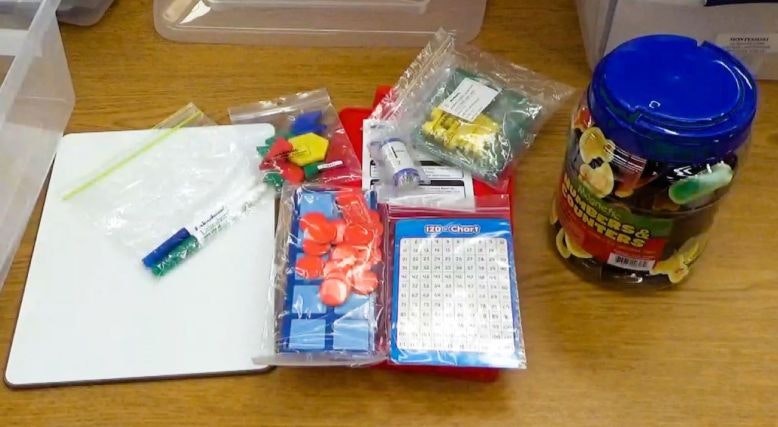 Assorted educational supplies on a table, including counters, a hundred chart, and a jar of numbers and counters.
