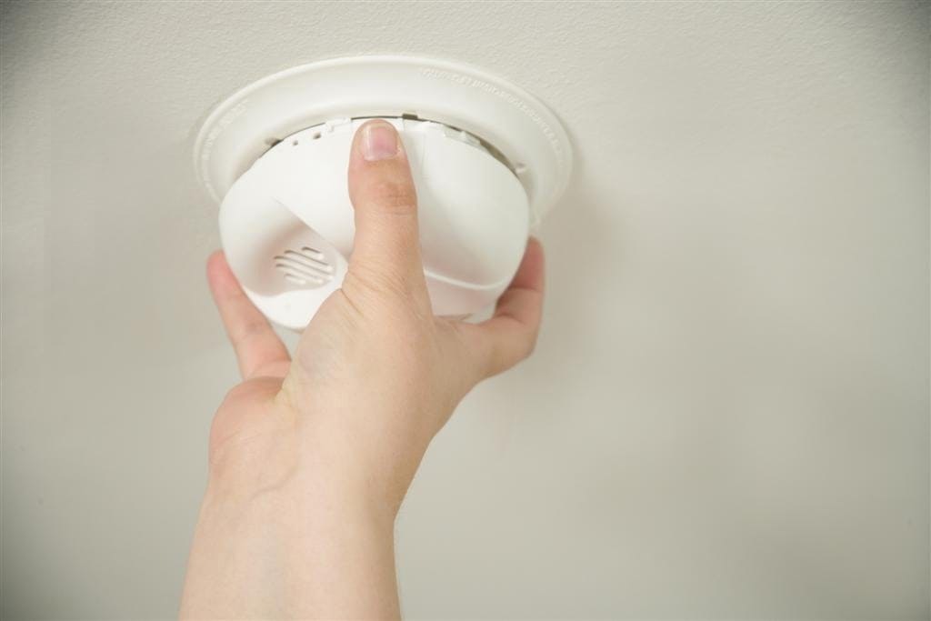 A hand installing a smoke detector on a ceiling.