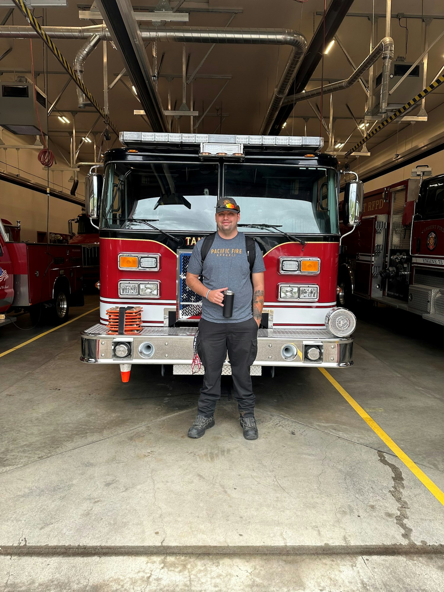 May contain: bumper, transportation, vehicle, clothing, footwear, shoe, hat, adult, male, man, person, fire truck, truck, standing, and cup