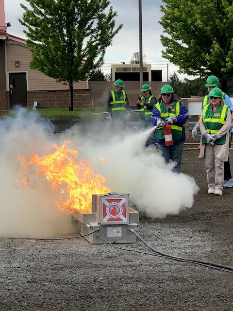 People in safety vests are conducting a fire extinguisher training with controlled flames.