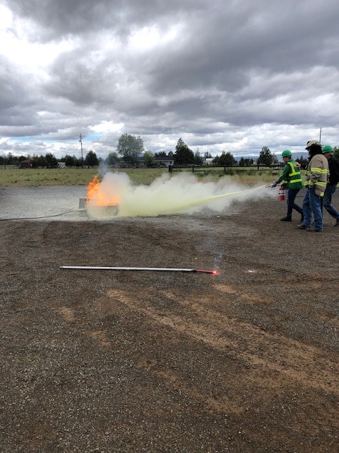 Two people with a fire extinguisher, a small fire, and smoke on a cloudy day. Image is tilted.