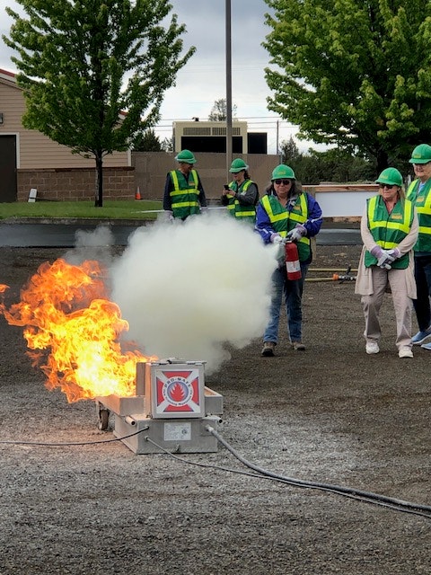 People in safety vests watch a fire extinguisher demonstration with a controlled blaze.