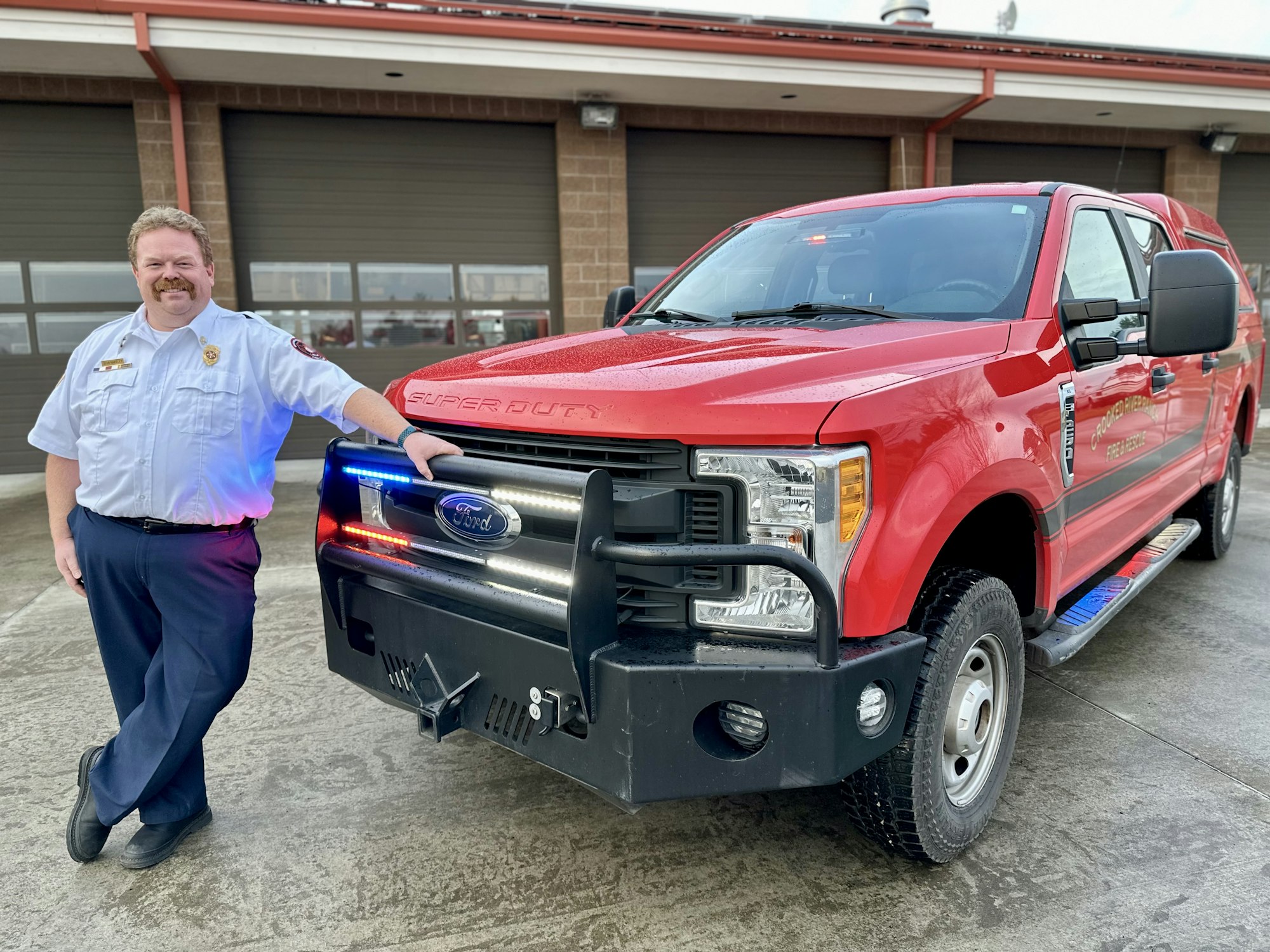 A man in a uniform leans against a red Ford Super Duty truck in front of garage doors.