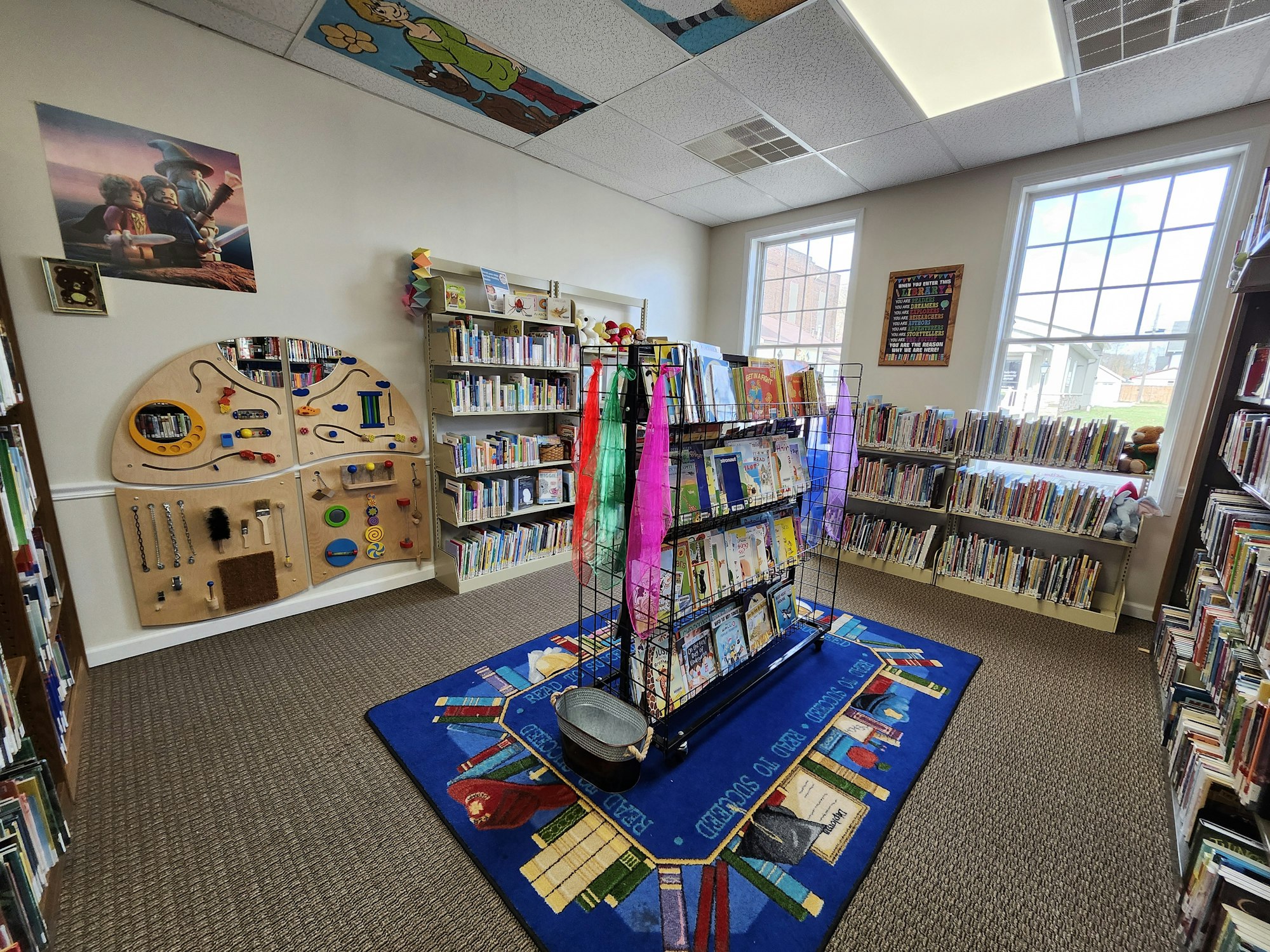 A children's section in a library with books, an activity wall, and colorful rugs.