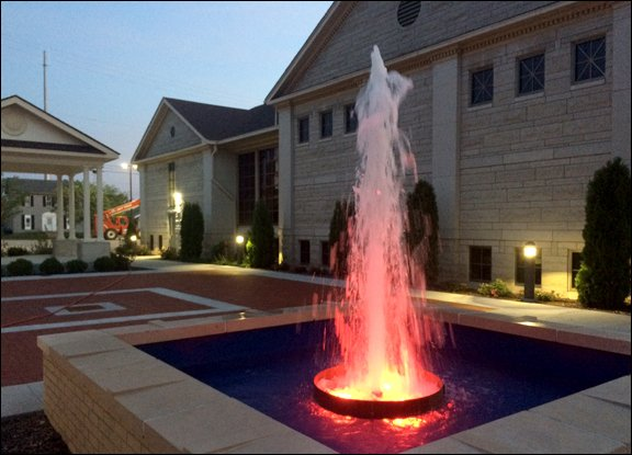 A lit fountain with red light at dusk, in front of a building with columns.