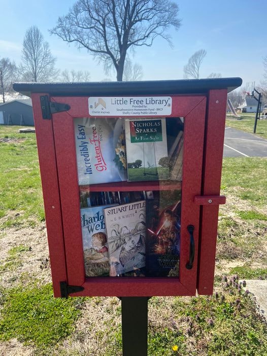 A Little Free Library box filled with books, outdoors on a sunny day.