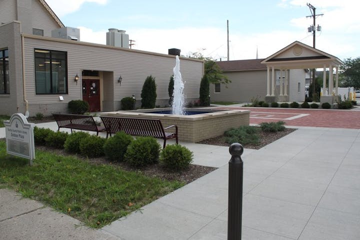 A courtyard with benches, a fountain, and buildings with a sign indicating a public library.
