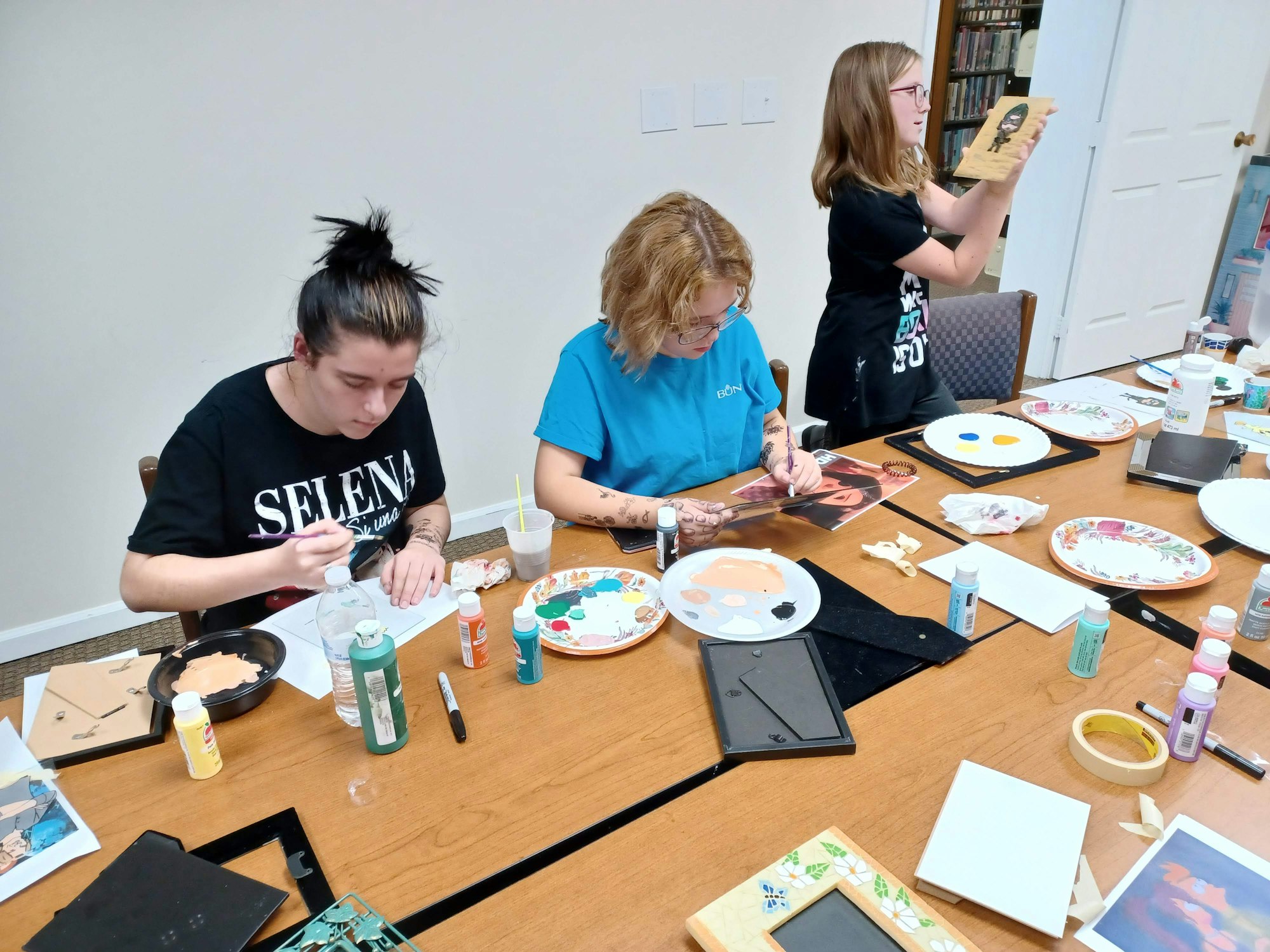 Three people participating in a craft activity, surrounded by paint and art supplies.