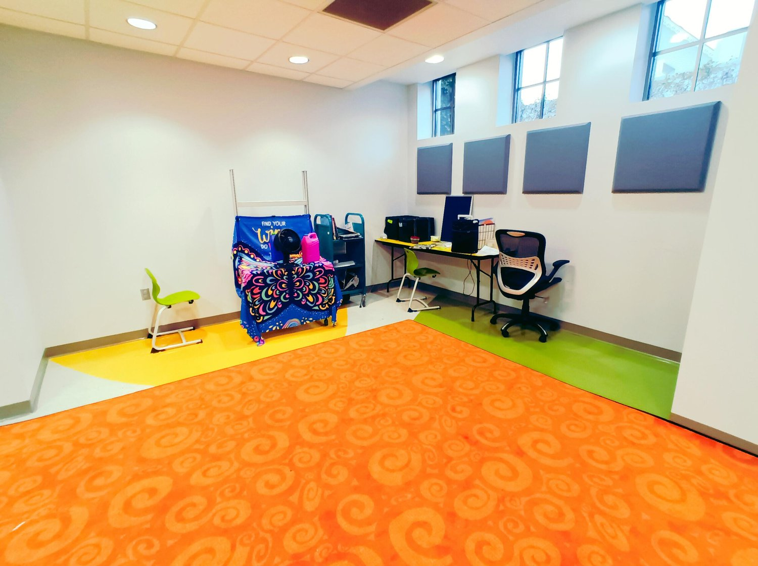 A colorful room with computers, desks, and a vibrant carpet, likely a modern classroom or a library nook.