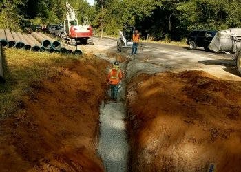Construction site with a trench for pipelines, workers, and machinery.