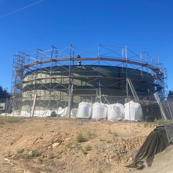 A water tower under construction with scaffolding, clear skies, and construction materials on the ground.