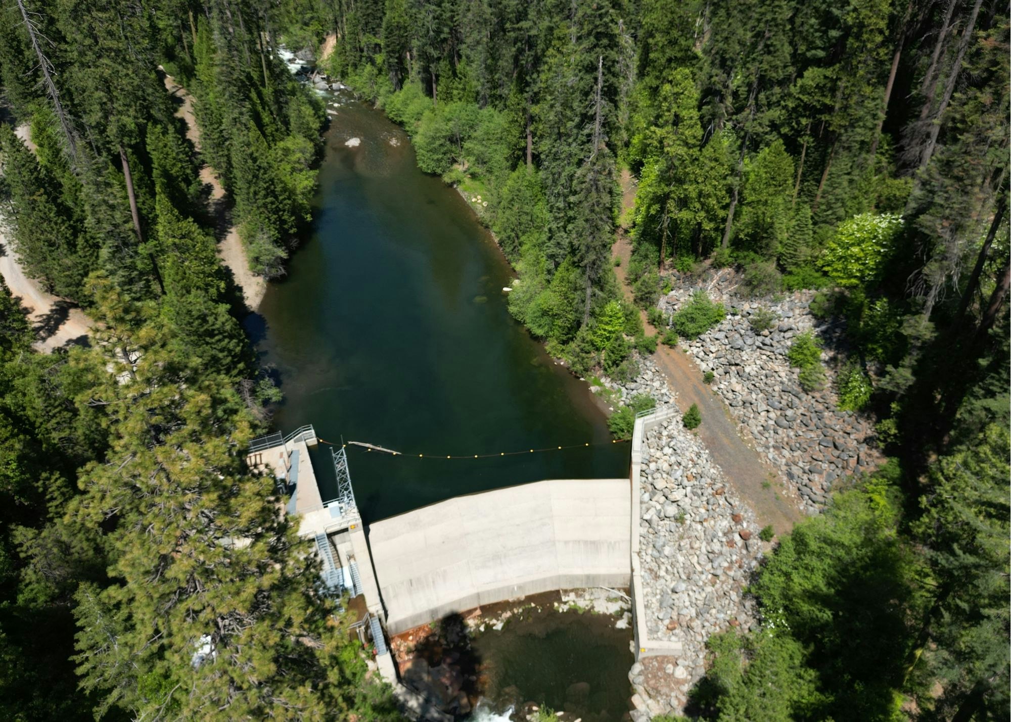 Aerial view of a dam with a river surrounded by dense forest and rocky terrain.