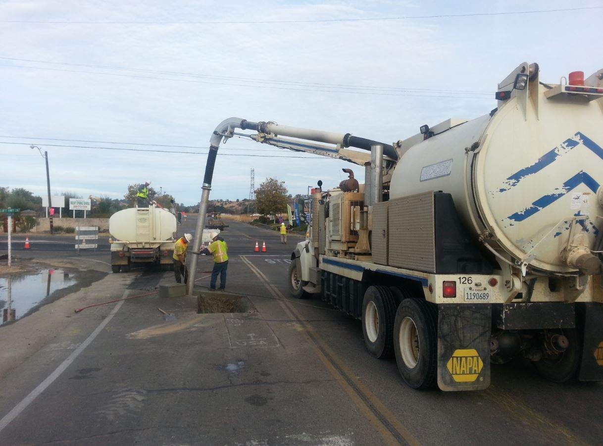 Construction work with a vacuum truck and workers on a road.