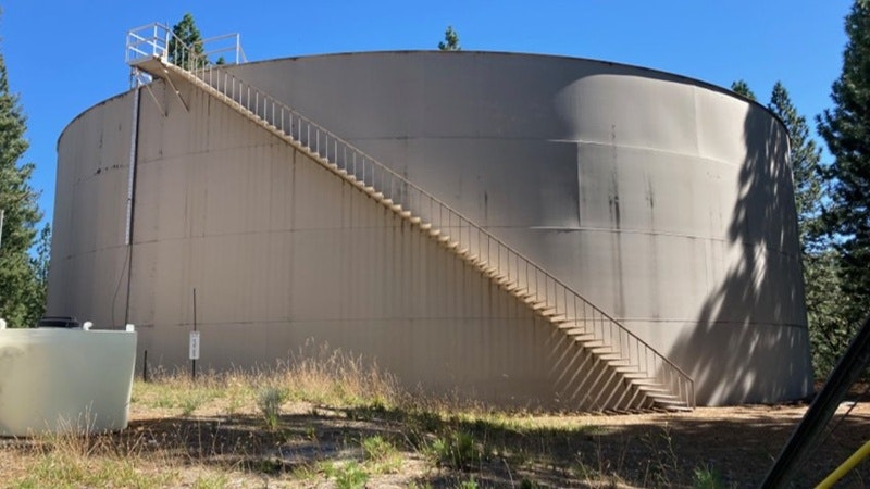A large cylindrical water tank with a metal staircase and surrounded by trees and grass.