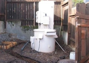 Outdoor construction site with a makeshift toilet setup using multiple white ceramic toilets placed on top of each other.
