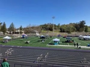 An outdoor sports field with tents, track lanes, and some people, under a clear sky.