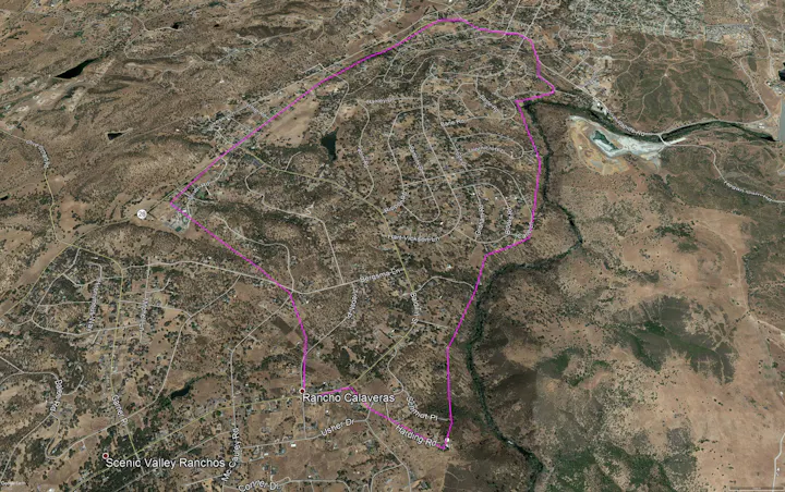 Satellite view showing a hilly terrain with roads and housing, outlined area possibly indicating a neighborhood or zone.